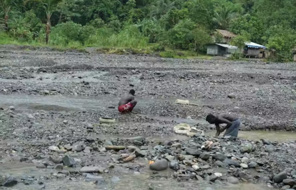 Two individuals are seen working in a rocky riverbed surrounded by lush greenery, highlighting the connection between the Bougainvilleans and their land.