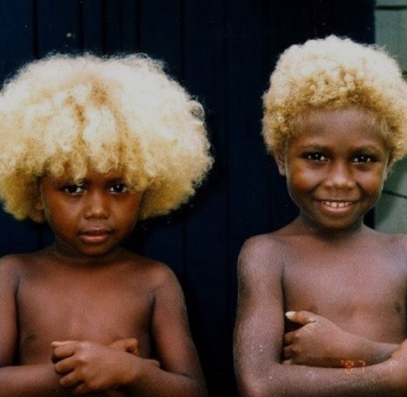Two children with natural blonde, curly hair standing in front of a dark background, showcasing their unique hairstyles and smiling expressions.